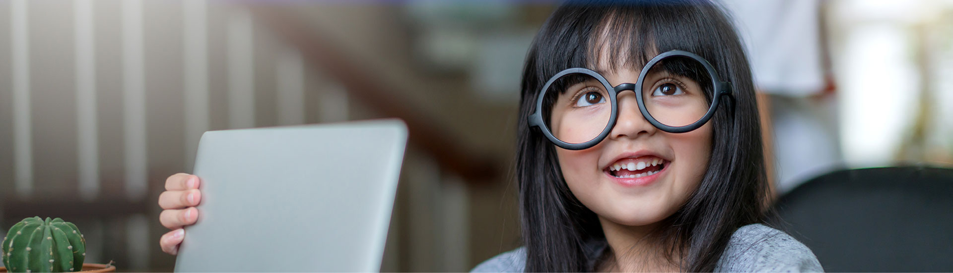 Imagem de uma garotinha, criança, de origem oriental, sorrindo em frente ao um notebook, com um olhar de quem esta com dúvidas